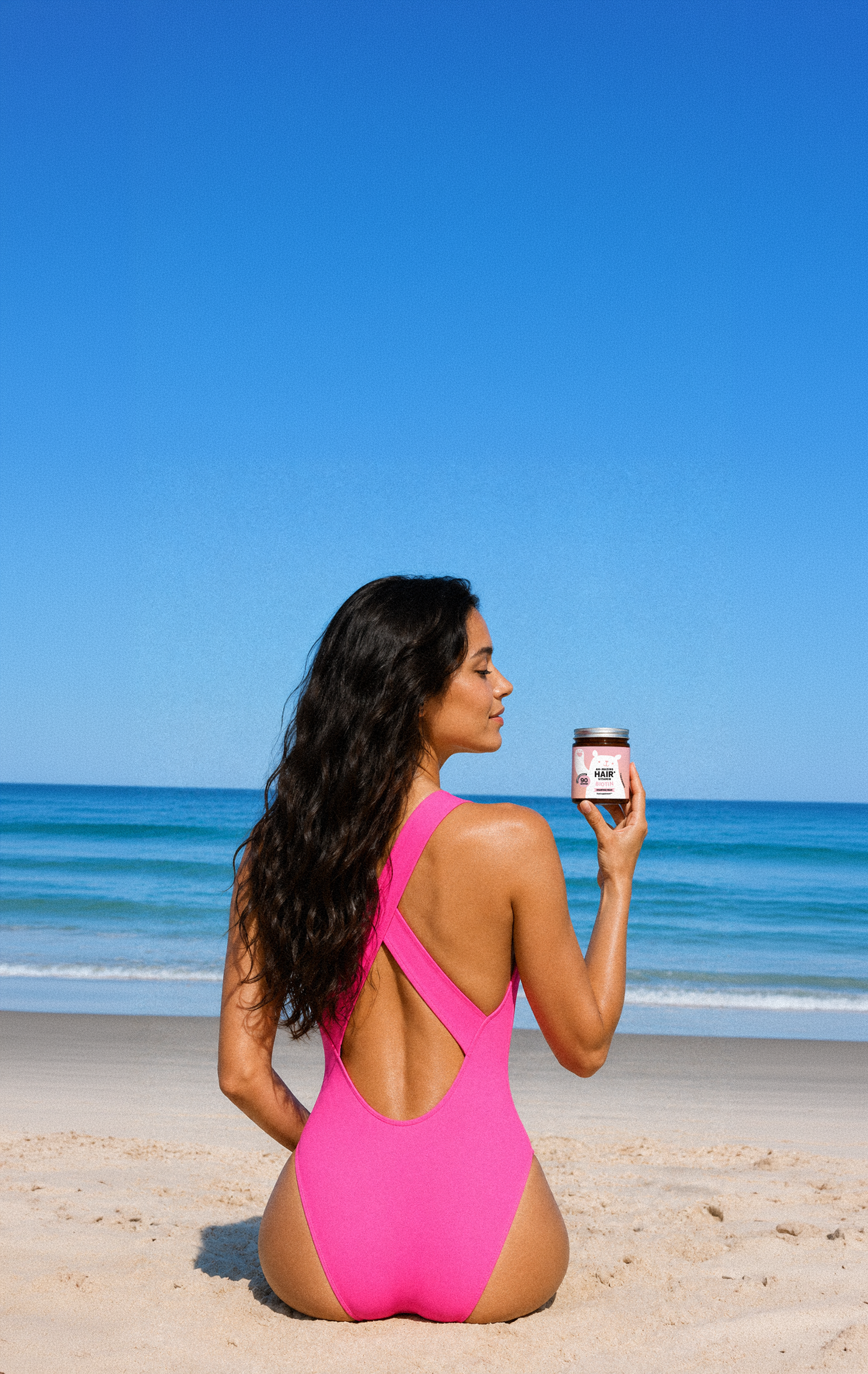 Model in a pink swimsuit holding a Hair and Biotin supplement jar at the beach.